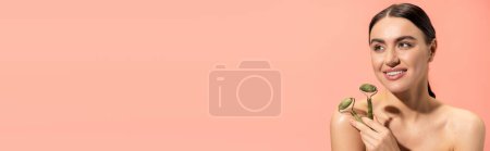 Téléchargez les photos : Happy woman with bare shoulders holding jade rollers isolated on pink, banner - en image libre de droit