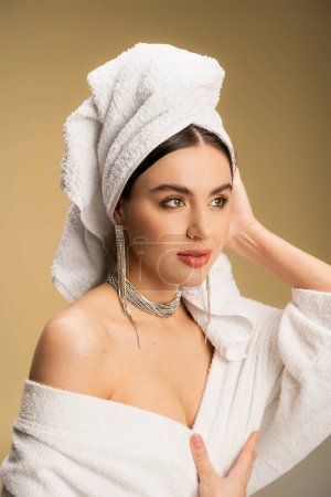 hübsche Frau in luxuriösem Schmuck posiert mit Handtuch auf dem Kopf auf beige 