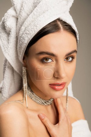 young woman in luxurious jewelry posing with towel on head isolated on grey