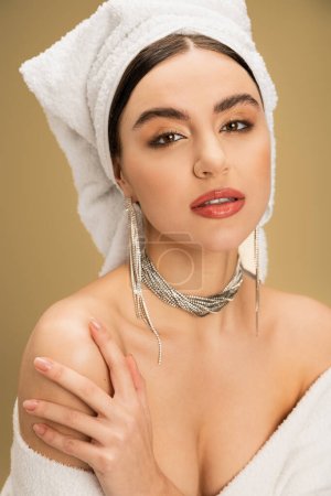 Téléchargez les photos : Élégante jeune femme avec maquillage et serviette sur la tête en regardant la caméra sur fond beige - en image libre de droit