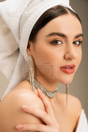 junge Frau mit Make-up und Handtuch auf dem Kopf blickt in die Kamera auf grauem Hintergrund 