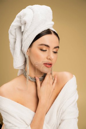 charming woman in jewelry with white towel on head touching chin on beige background 