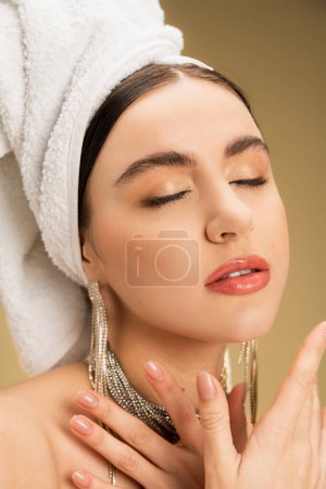Foto de Close up view of charming woman in jewelry with white towel on head posing on beige background - Imagen libre de derechos