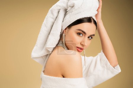 femme brune avec maquillage touchant serviette blanche sur la tête sur fond beige 
