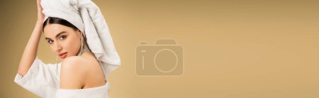 brunette woman with makeup touching white towel on head on beige background, banner 
