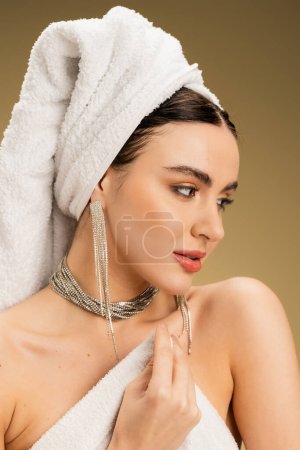retrato de mujer encantadora en joyería sosteniendo toalla blanca sobre fondo beige 