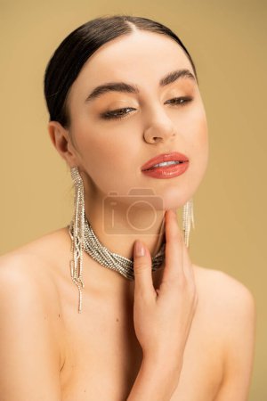 sensual woman in necklace and earrings touching neck isolated on beige 