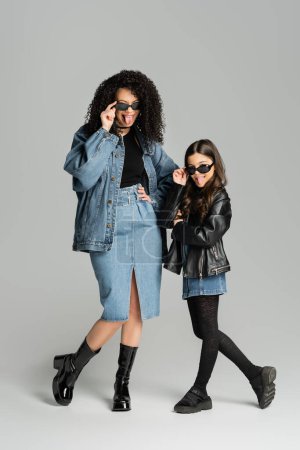 Foto de Fashionable mom and daughter in sunglasses sticking out tongues on grey background - Imagen libre de derechos