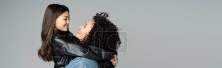 Téléchargez les photos : Side view of smiling kid in leather jacket hugging curly mom isolated on grey, banner - en image libre de droit