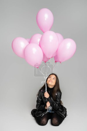 Photo for Cheerful and stylish girl looking at pink balloons on grey background - Royalty Free Image