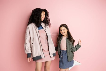 Téléchargez les photos : Trendy preteen child looking at camera near mother on pink background - en image libre de droit