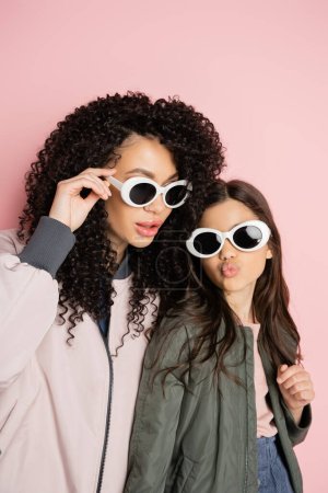 Photo for Preteen girl in sunglasses pouting lips near curly mom on pink background - Royalty Free Image