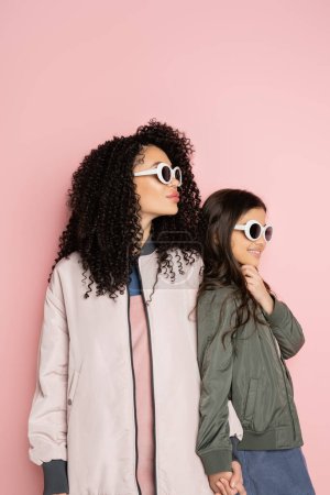 Trendy woman and girl in sunglasses and bomber jackets on pink background 