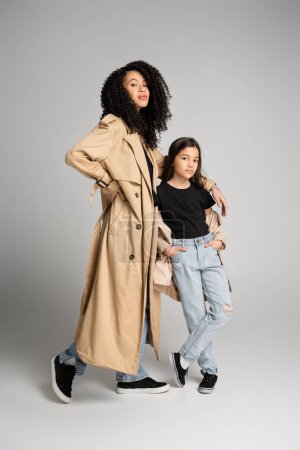Téléchargez les photos : Pleine longueur de mère et fille élégantes en trench manteaux posant sur fond gris - en image libre de droit