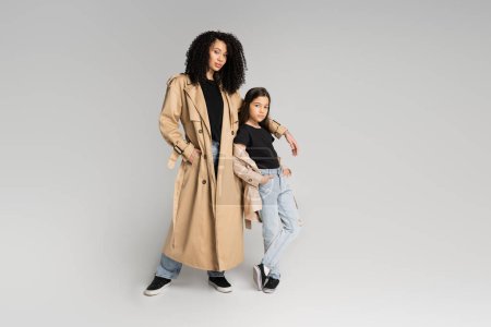 Téléchargez les photos : Fashionable mother and daughter in trench coats posing on grey background - en image libre de droit