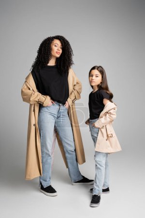 Téléchargez les photos : Preteen child in trench coat posing near stylish mom on grey background - en image libre de droit