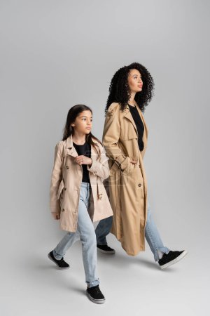 Téléchargez les photos : Mère et fille branchées en trench-coat marchant sur fond gris - en image libre de droit