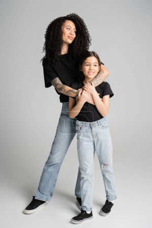 Trendy mother hugging kid in jeans and t-shirt on grey background 
