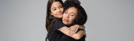Preteen kid in t-shirt hugging curly mom isolated on grey, banner 