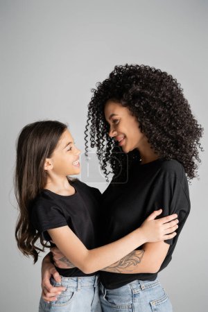 Téléchargez les photos : Vue latérale de la femme et de la fille positives en t-shirts noirs câlins isolés sur gris - en image libre de droit