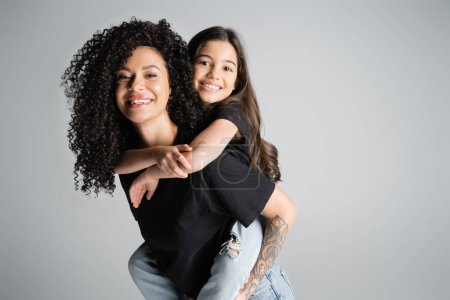 Téléchargez les photos : Gai fille piggybackking sur bouclé tatoué mère isolé sur gris - en image libre de droit