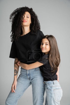 Stylish woman hugging preteen daughter isolated on grey 