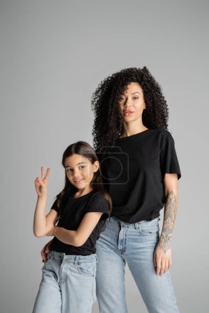 Preteen kid showing peace sign near stylish mom isolated on grey 