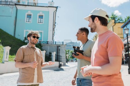 guía turístico alegre gesto durante la excursión con viajeros multiétnicos en el descenso de Andrews en Kiev en el día de verano