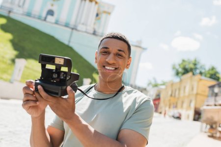 Unbekümmerter afrikanisch-amerikanischer Tourist mit Oldtimer-Kamera lächelt bei Andrews-Abfahrt in Kiew