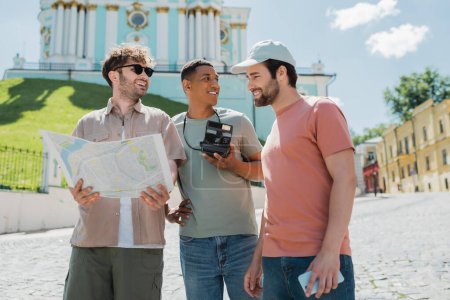 Ein fröhlicher Reiseleiter mit Sonnenbrille hält eine Karte in der Nähe von Reisenden auf der Andreasabfahrt in Kiew