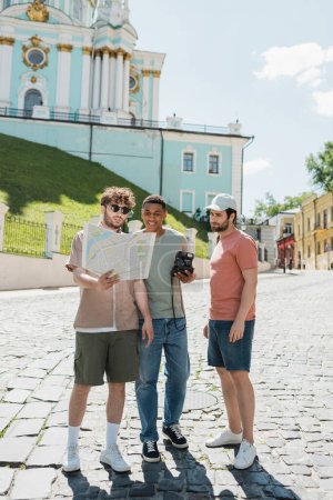 Junge Reiseleiterin schaut auf Stadtplan in der Nähe von unbeschwerten Touristen beim Andreasabstieg in Kiew