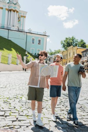 full length of multiethnic tourists walking with tour guide holding travel map and pointing with hand on Andrews descent in Kyiv
