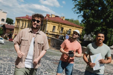 turistas multiétnicos positivos con cámara vintage y mapa sonriendo durante la excursión con guía turístico en el descenso de Andrews en Kiev