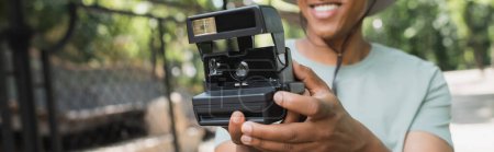 Téléchargez les photos : Vue partielle du voyageur afro-américain flou avec caméra vintage prenant des photos dans le parc, bannière - en image libre de droit
