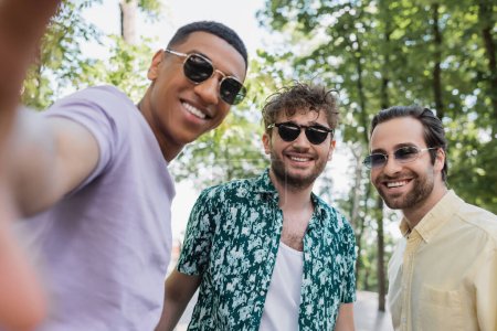 Fröhliche multiethnische Freunde mit Sonnenbrille stehen im Sommer im Park 