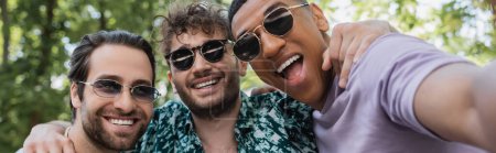 Fröhliche multiethnische Freunde mit Sonnenbrille, die sich im Sommerpark umarmen, Banner 