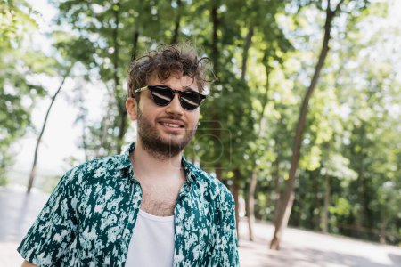 Lächelnder Mann in lässiger Kleidung und Sonnenbrille im Sommerpark 