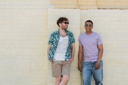 Positive interracial friends in sunglasses standing near building in Kyiv 