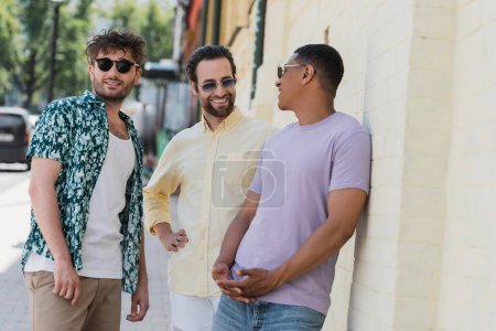 Positive multiethnische Freunde mit Sonnenbrille unterhalten sich auf der Straße in Kiew 