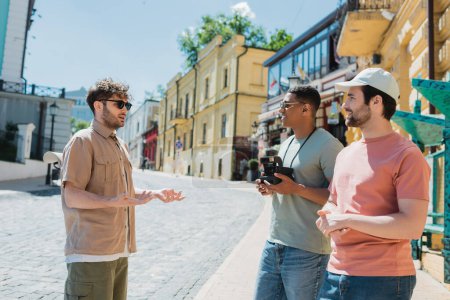 Guide im Gespräch mit interrassischen Freunden mit Retro-Kamera auf Podil in Kiew im Sommer 