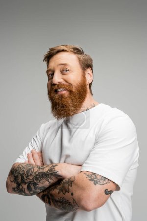 Homme tatoué insouciant croisant les bras isolé sur gris 