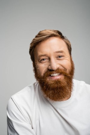 Portrait of overjoyed bearded man looking at camera isolated on grey 
