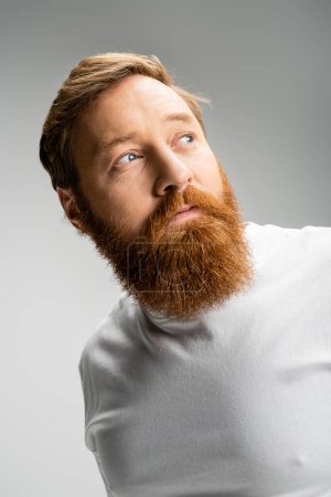 Portrait of bearded man in t-shirt looking away isolated on grey 