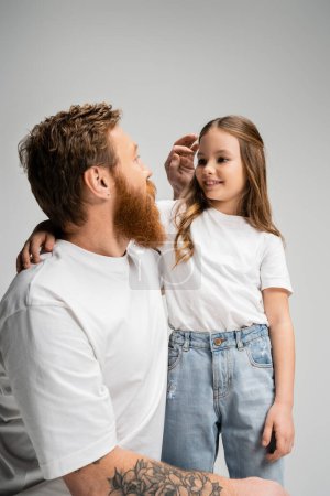 Bärtiger Vater stellt Haare lächelnder Tochter auf grau 