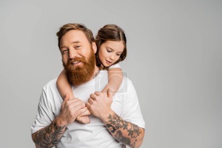 Preteen girl umarmt tätowierte und glückliche Vater isoliert auf grau 