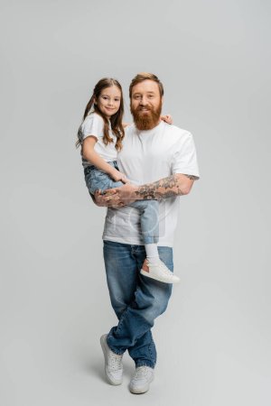 Ganzer positiver Vater in T-Shirt und Jeans mit Tochter auf grauem Hintergrund
