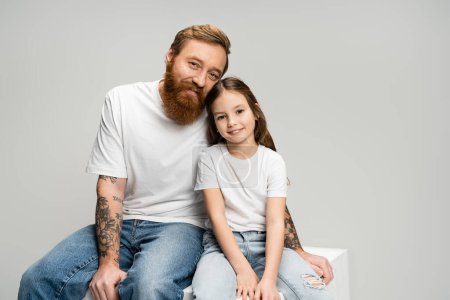 Téléchargez les photos : Homme tatoué positif assis près de la fille sur cube isolé sur gris - en image libre de droit