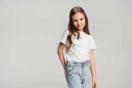 Portrait of positive child posing and looking at camera isolated on grey  