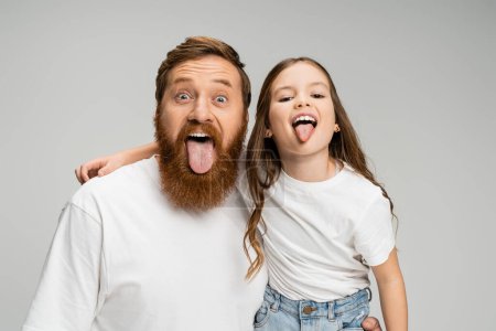 Preteen kid and bearded dad sticking out tongues isolated on grey  