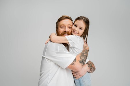 Bärtiger Mann umarmt unbeschwerte Tochter und blickt vereinzelt in die Kamera  